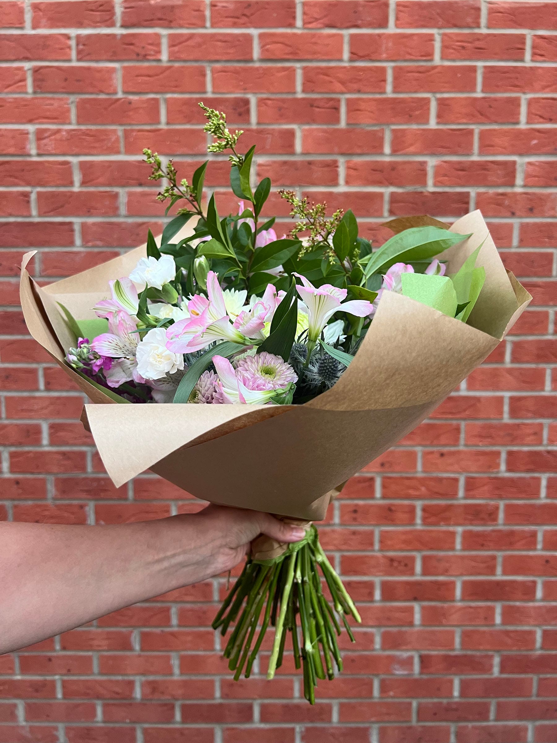 Hand holding bouquet against brick wall