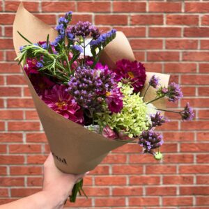Hand holding colourful flower bouquet against brick wall.