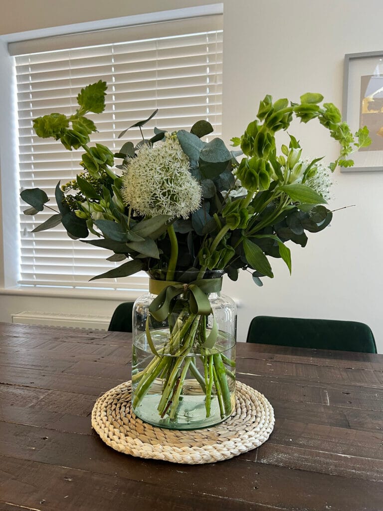 Green floral bouquet in glass jar on wooden table.